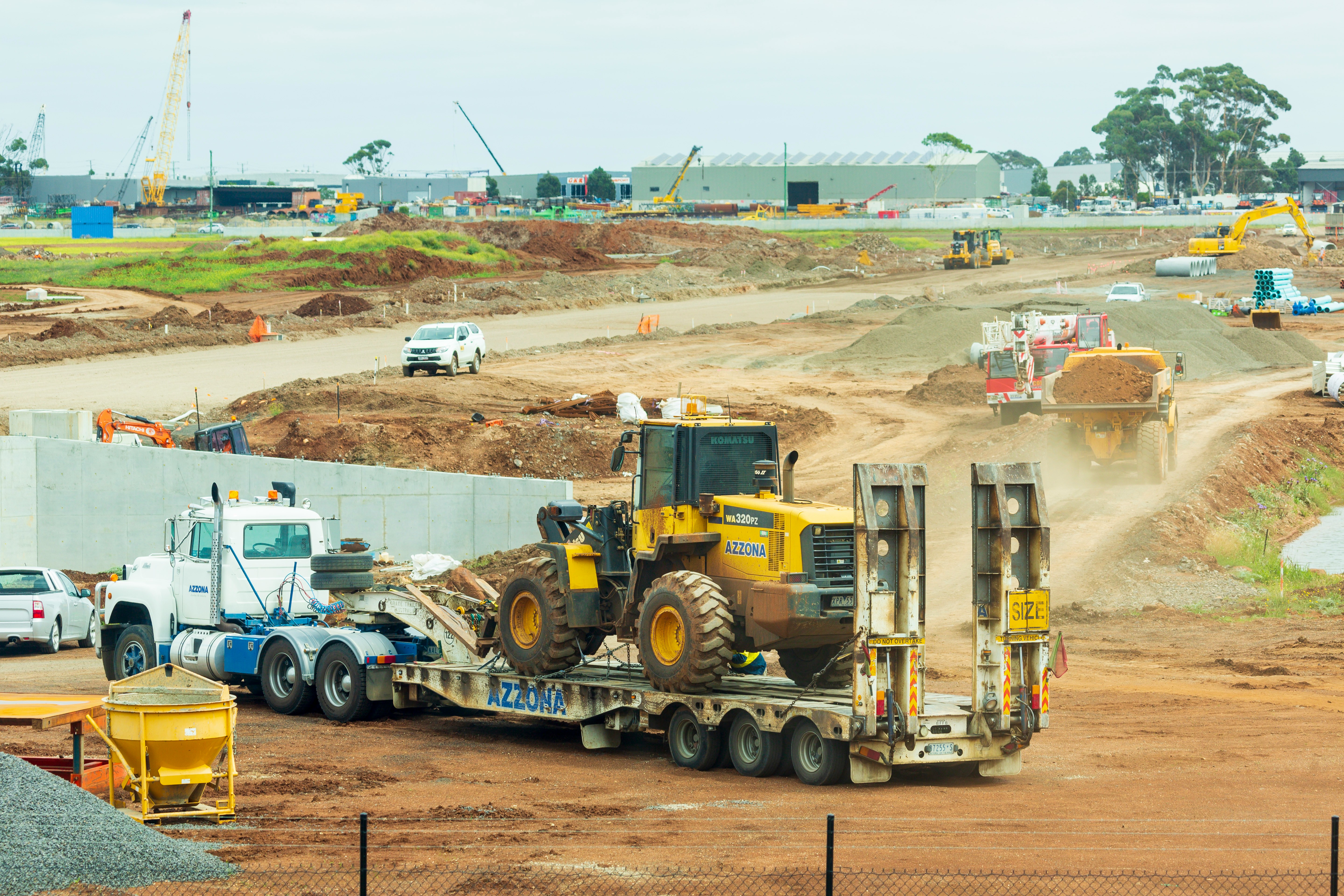 Flatbed truck transporting a Komatsu WA320PZ wheel loader on a construction site, illustrating safe and efficient heavy equipment transportation practices.